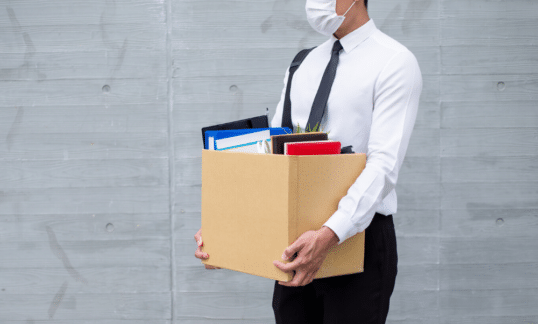 An employee laid off due to Covid-19 leaves his office with his belongings in a box.