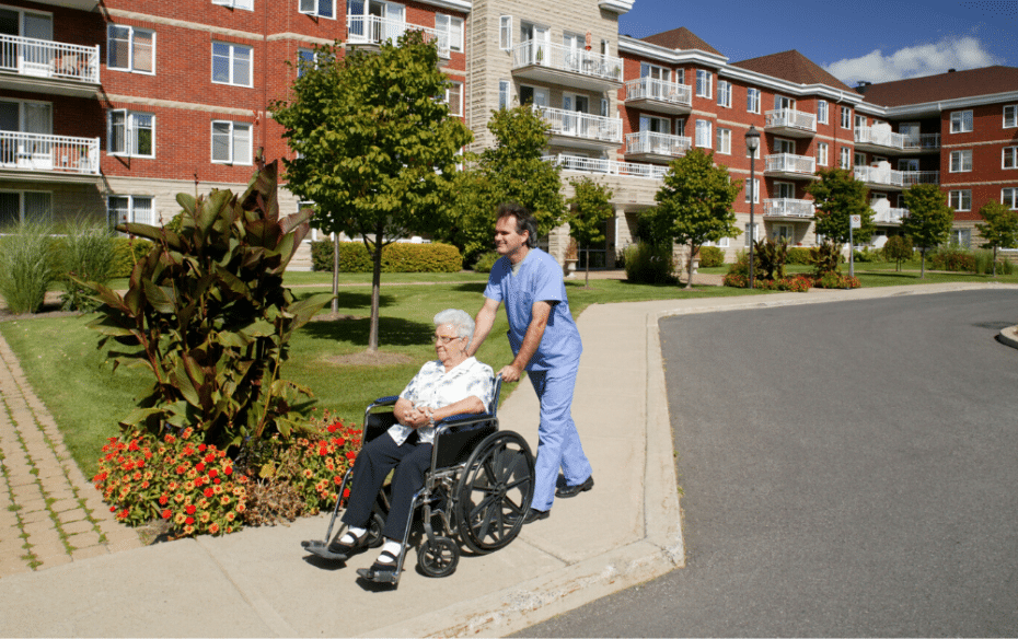 An elderly woman being pushed in a wheelchair by a staff member at a long term care home.