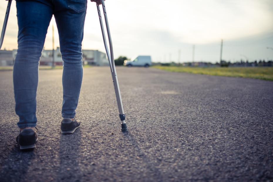 man walking with crutches at sunset. rear view