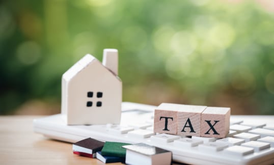 A model house model is placed on wooden blocks spelling TAX