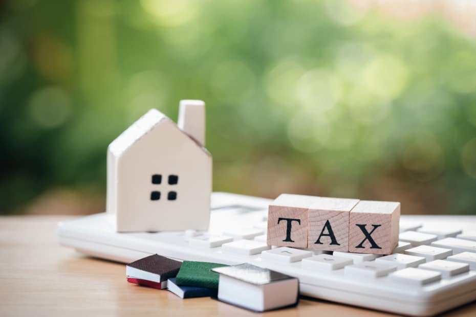 A model house model is placed on wooden blocks spelling TAX