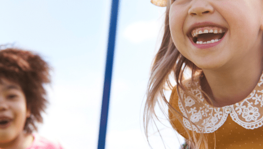 Two girls on a playground swingset.