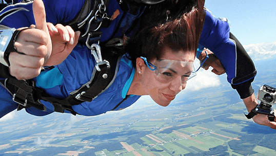 Woman sky diving over green fields.