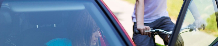 women waits to open her car door as a biker passes her vehicle on the road.