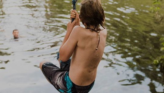Young boy swings on rope into jump into a lake