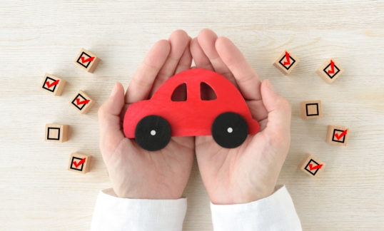 Car toy covered by human's hands surrounded by wooden blocks with checking marks