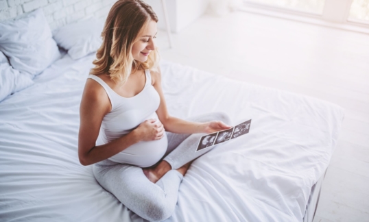 Pregnant woman is sitting in bed with ultrasonography in hands. Last months of pregnancy.