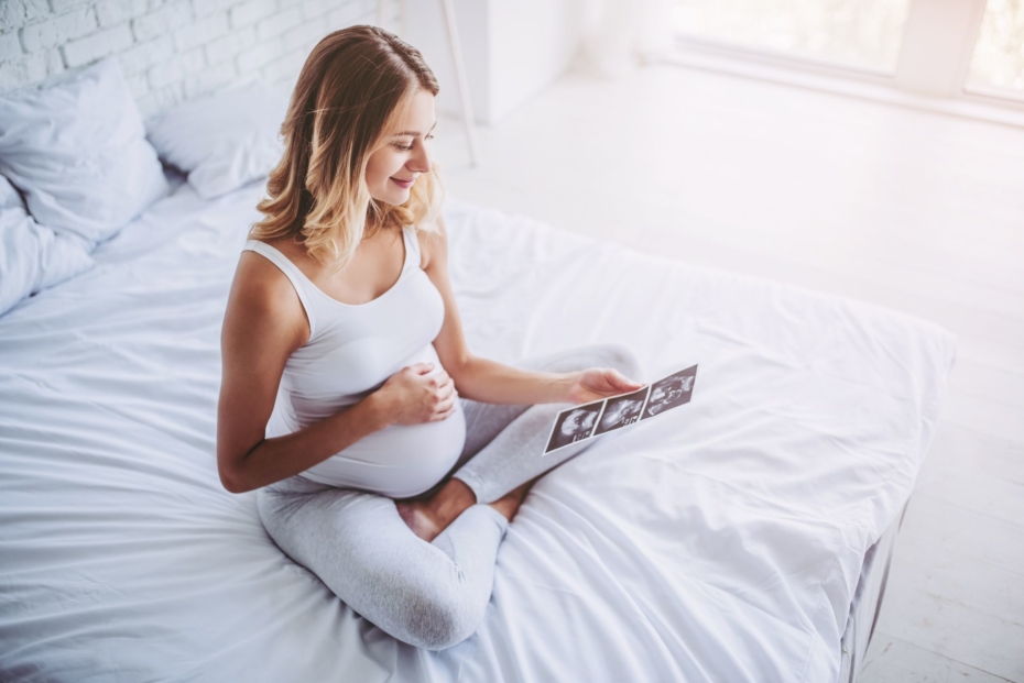 Pregnant woman is sitting in bed with ultrasonography in hands. Last months of pregnancy.