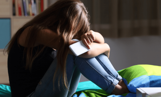 A young girl and cyberbully victim crying and holding a cellphone.