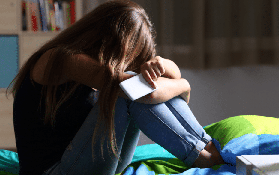 A young girl and cyberbully victim crying and holding a cellphone.