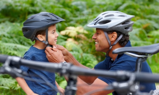 Caring father helping son put on bicycle helmet - Outdoors