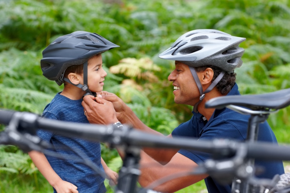 Caring father helping son put on bicycle helmet - Outdoors