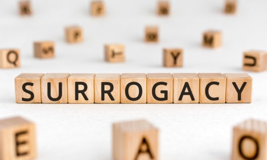 Surrogacy - word from wooden blocks with letters, a surrogate mother surrogacy concept, random letters around white background