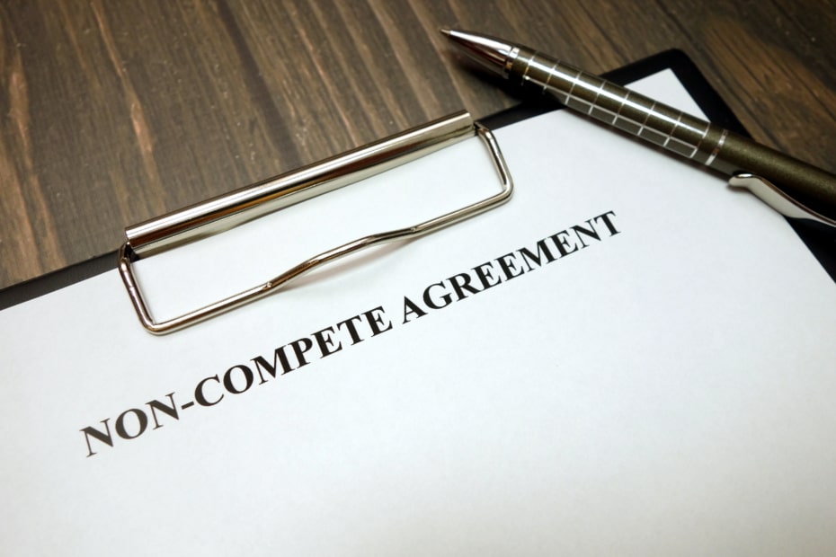 Clipboard with non-compete agreement and pen on wooden desk background