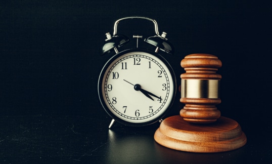 Wooden judge hammer with alarm clock on black background