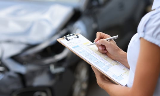 Photo of insurance agent with a ruined car in the background.