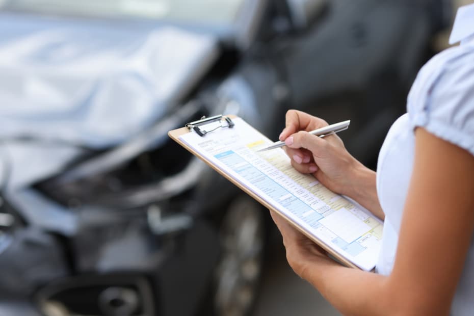 Photo of insurance agent with a ruined car in the background.