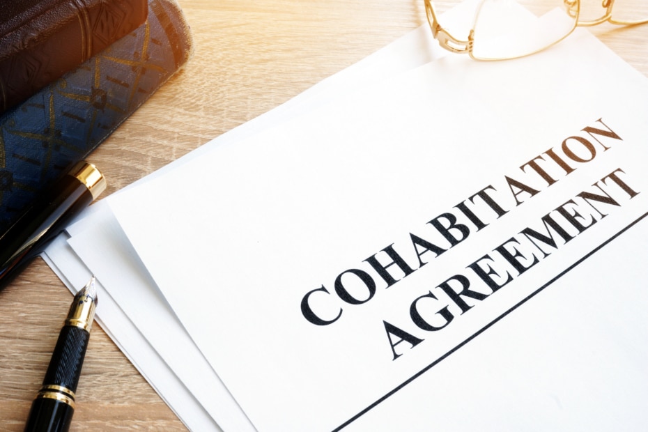 Paper document on a wood surface next to glasses, books, and a black pen. The paper has large black leaders reading Cohabitation Agreement.