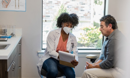 Doctor and man looking at clipboard and talking.