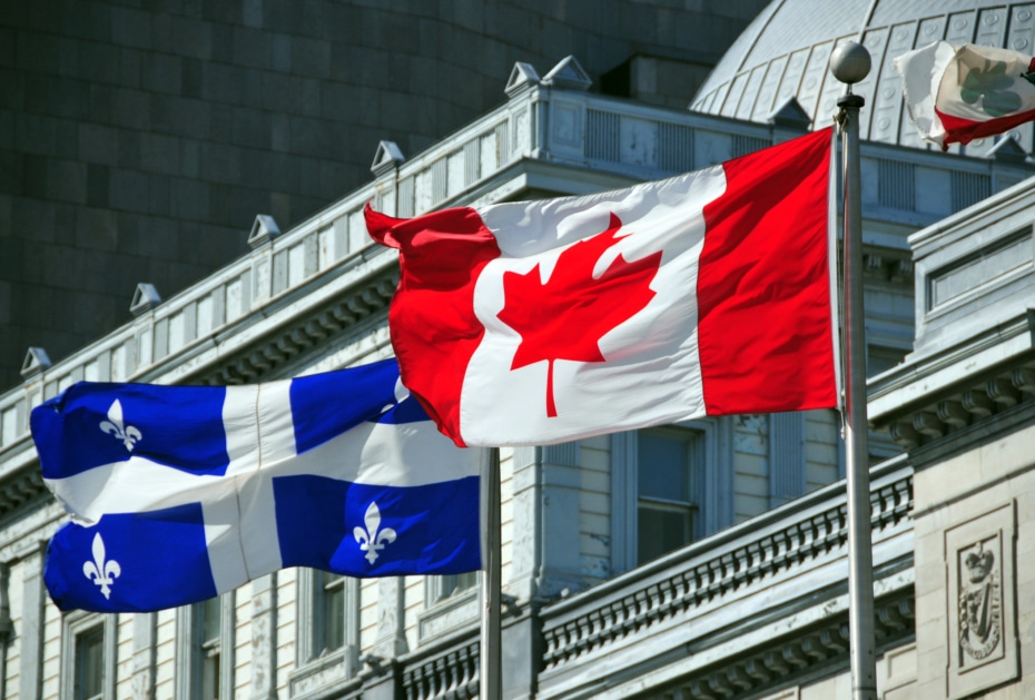 Quebec flag and Canada flag in flying in the wind in front of a building.